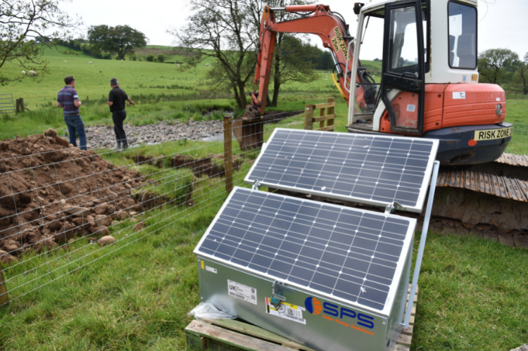 A solar powered water pump unit sitting in front of a digger with two men in the background discussing where to situate the plant next to a water course.